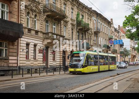 LEMBERG, UKRAINE - 20. Juni 2021: Eine lebhafte Straßenbahn fährt entlang einer kopfsteingepflasterten Straße, die von historischen Gebäuden umgeben ist. Die Stadt verströmt Charme mit kunstvoller Architektur und lebhafter Atmosphäre an einem bewölkten Tag. Stockfoto
