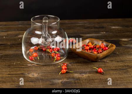 Hagebuttenfrüchte auf einem schwarzen Teetisch, eine Ernte frischer roter Früchte aus einer Rose, die zur Zubereitung von Tee in einer Teekanne aus Glas verwendet werden Stockfoto