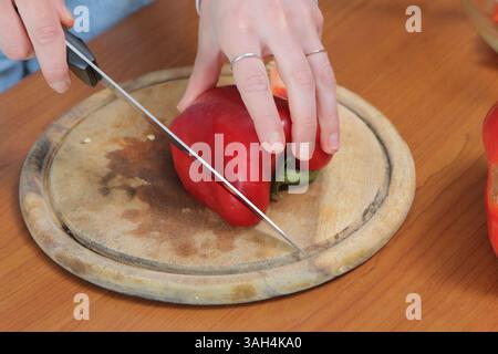 Frau schneidet eine rote Paprika auf einem hölzernen Schneidebrett und bereitet Zutaten für eine gesunde Mahlzeit vor Stockfoto