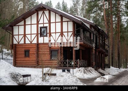 Großes zweistöckiges braunes Gästehaus aus Holz mit Balkon vor winterlicher Waldkulisse. Stockfoto