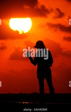 Isle Of Palms, Usa. April 2025. Eine Frau sieht zu, wie die Sonne über dem Atlantischen Ozean steigt, die Silhouette an einem bewölkten Morgen am Wild Dunes Beach am 9. April 2025 in Isle of Palms, South Carolina. Eine kalte Front zog über Nacht durch das lowcountry und fiel die Temperaturen von den 80er auf saisonale 60er Jahre Quelle: Richard Ellis/Richard Ellis/Alamy Live News Stockfoto