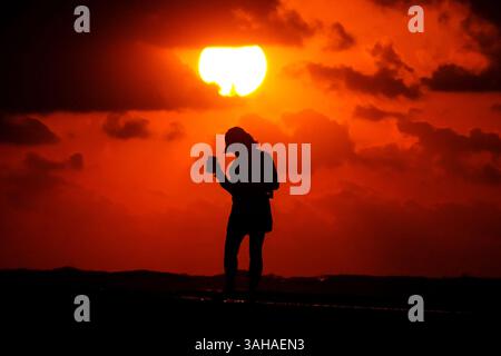 Isle Of Palms, Usa. April 2025. Eine Frau sieht zu, wie die Sonne über dem Atlantischen Ozean steigt, die Silhouette an einem bewölkten Morgen am Wild Dunes Beach am 9. April 2025 in Isle of Palms, South Carolina. Eine kalte Front zog über Nacht durch das lowcountry und fiel die Temperaturen von den 80er auf saisonale 60er Jahre Quelle: Richard Ellis/Richard Ellis/Alamy Live News Stockfoto