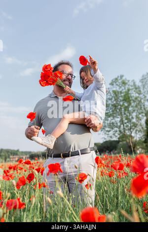 Vater hält eine kleine Tochter in Händen, die mitten in einem großen Mohnfeld steht Stockfoto