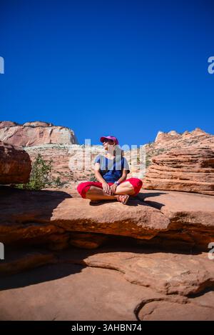 Junge kaukasische Frau sitzt mit überkreuzten Beinen auf dem Canyon Overlook Trail im Zion National Park, Utah Stockfoto