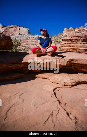 Junge kaukasische Frau sitzt mit überkreuzten Beinen auf dem Canyon Overlook Trail im Zion National Park, Utah Stockfoto