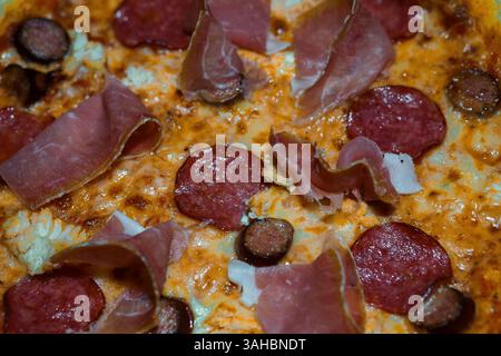 Nahaufnahme einer köstlichen Pizza mit Peperoni, Schinken und geschmolzenem Käse mit reichhaltiger Textur und appetitlichen Aromen. Stockfoto