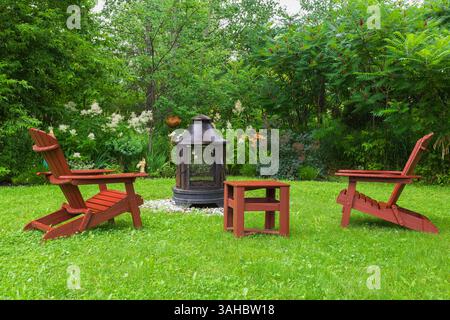 Rote hölzerne Adirondack-Stühle und Holzpagode aus Stahl auf grünem Gras und umgeben von Persicaria polymorpha - Riesenblumen aus weißem Fleece, o Stockfoto