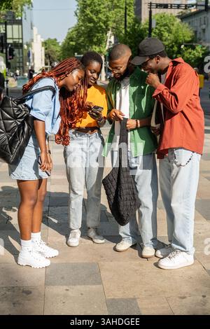 Verschiedene afroamerikanische Studentenfreunde diskutieren über Pläne auf Smartphones und entscheiden, wo sie abhängen sollen Stockfoto