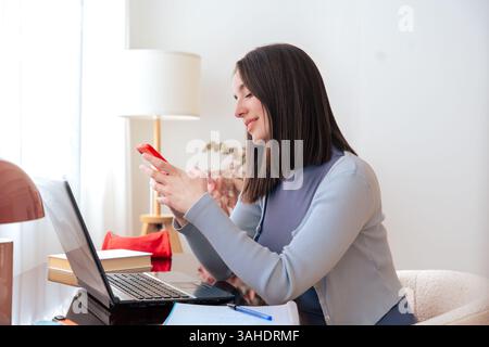 Frau, die zu Hause mit dem Smartphone arbeitet, Multitasking und lächelnd Stockfoto