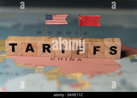Holzblöcke, die das Wort ZÖLLE auf einer Weltkarte über China bilden, mit kleinen US- und China-Flaggen, die Handelspolitik repräsentieren Stockfoto