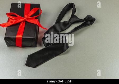 Eine schwarze Krawatte liegt neben einem wunderschön gewickelten Geschenk mit einem roten Band, perfekt für Vatertag oder eine Geburtstagsfeier. Ein Symbol für Appreci Stockfoto
