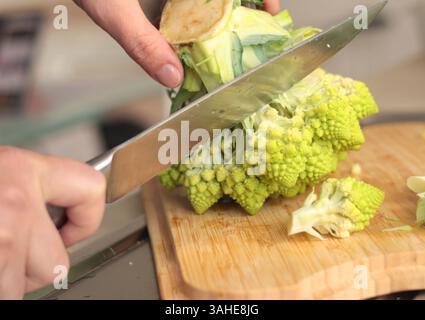 Anonymes Schneiden von Romesco-Brokkoli-Sprossen mit Messer auf Holzbrett in der Küche. Gesunde Ernährung. Lebensmittel und grünes Gemüse. Stockfoto