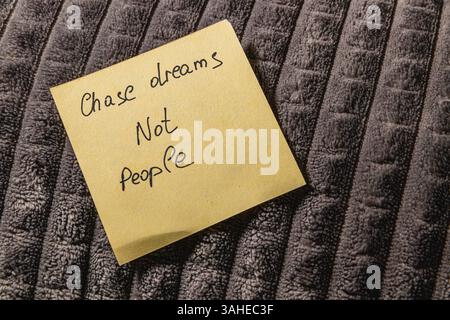 Eine Haftnotiz mit einer motivierenden Nachricht wird auf einer weichen, dunklen Stoffoberfläche platziert. Die Notiz fordert die einzelnen dazu auf, sich auf die Verwirklichung ihrer Träume zu konzentrieren Stockfoto