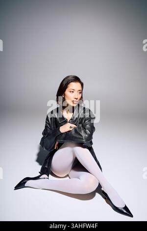 Eine stilvolle junge Frau sitzt anmutig auf dem Boden und zeigt ihr modisches Outfit. Stockfoto