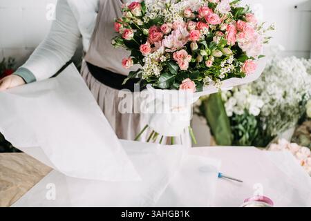 Florist präsentiert einen fertigen Blumenstrauß aus rosa Blumen, gewickelt in knusprigem weißem Papier. Blumenpräsentation, Blumenverpackung, Öko-Blumenschmuck Stockfoto