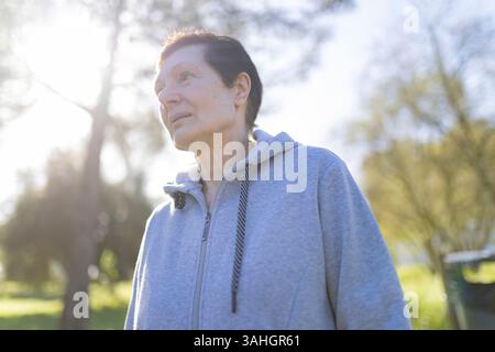 Seniorin genießt Sonnenlicht im grünen Park: Die Schönheit der Natur betrachten Stockfoto
