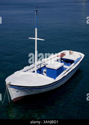 Weißes Boot auf klarem blauem Wasser mit einem Mann, der vorne unter klarem Himmel sitzt. Stockfoto