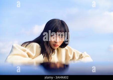 Eine junge Frau in einem weißen Pullover, die aufmerksam vor dem Hintergrund des Himmels schaut. Brandenburg, Deutschland Stockfoto