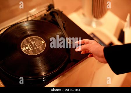 Die Hand reicht, um die Nadel auf schwarzem Vinyl auf den Plattenspieler in einem warmen Raum zu legen. Stockfoto