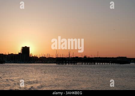9. April 2025 - Portsmouth, Großbritannien - Sonnenuntergang über Gosport und Portsmouth Harbour, mit Segelyachtmasten am Horizont. Stockfoto