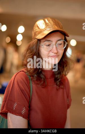 Frau in rotem Hemd und goldener Mütze mit Brille im Innenbereich beim Einkaufen. Stockfoto