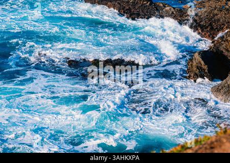 Wellen krachen gegen felsige Klippen mit leuchtend blauem und weißem schaumigem Wasser. Monterey, CA, USA Stockfoto