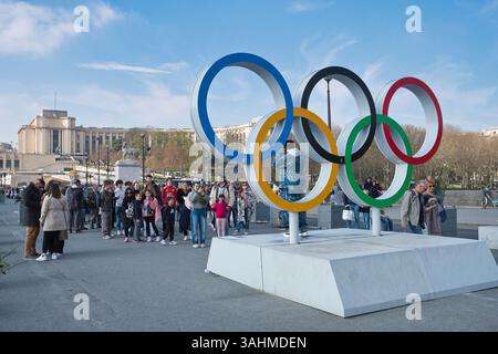 Touristen stehen an, um sich im Frühjahr vor den Olympischen Ringen am Eiffelturm in Paris fotografieren zu lassen Stockfoto
