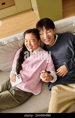 Ein junges asiatisches Paar liegt gemütlich auf der Couch und teilt Lächeln und Lachen. Stockfoto