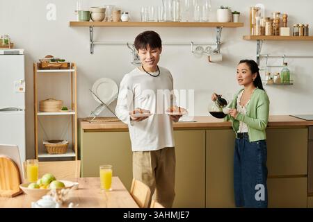 Ein glückliches junges asiatisches Paar genießt hausgemachtes Frühstück zusammen in ihrer einladenden Küche. Stockfoto