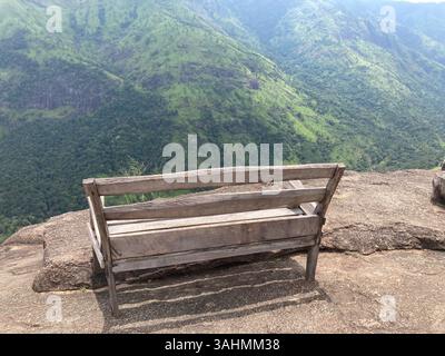 Eine hölzerne Bank auf felsigen Höhen, umgeben von Bäumen und ruhiger Brise, ist der perfekte Ort, um zu pausieren und zu atmen. Stockfoto