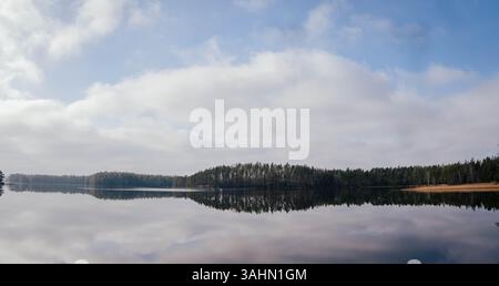 A serene lake in Sweden, featuring an island surrounded by lush trees, with a stunning reflection on the calm water. The peaceful and tranquil scene c Stockfoto