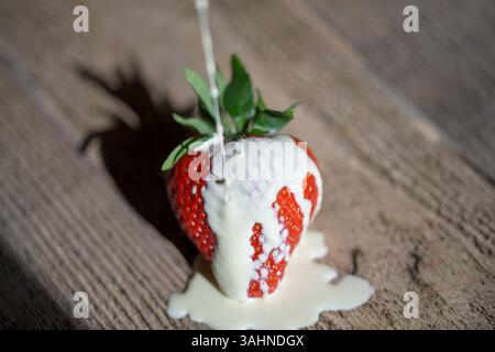 Einzelne Erdbeere (Fragaria x Ananassa) mit Creme auf rustikalem Holz, symbolisiert Sommerdesserts, Genießen und frische saisonale Speisen Stockfoto