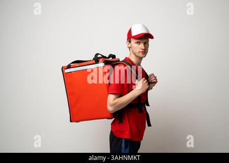 Junger Liefermann in roter Uniform mit Thermalrucksack. Fastfood-Lieferservice. Stockfoto