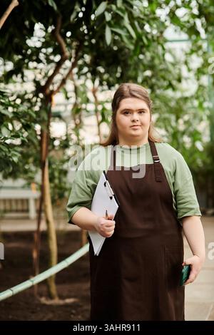 In einem üppigen Gewächshaus zeigt eine selbstbewusste junge Frau ihr Engagement für die Pflanzen. Stockfoto