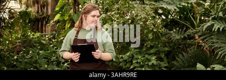 Eine junge Frau mit Down-Syndrom zeigt ihr Selbstvertrauen, während sie in einem üppigen Gewächshaus arbeitet. Stockfoto
