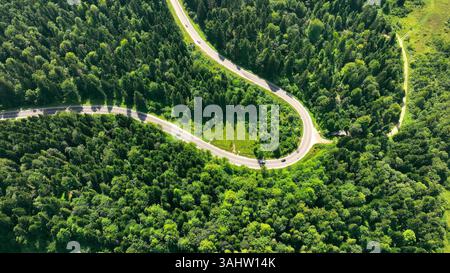 Blick aus der Vogelperspektive auf die Serpentine Road durch den üppigen Wald. Eine kurvige Serpentinenstraße, die durch dichten, üppig grünen Wald mit verstreuten Fahrzeugen führt. Stockfoto