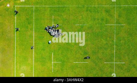 Luftaufnahme von Rugby Scrum auf Green Field. Eine Luftaufnahme eines laufenden Rugby-Spiels von oben nach unten, die eine Scrum-Formation auf einem leuchtenden Grün hervorhebt Stockfoto