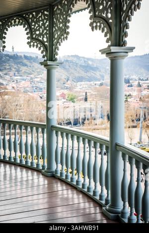 Schöner traditioneller georgianischer Balkon mit geschnitzten Holzelementen und Panoramablick auf die Altstadt von Tiflis und die Hügel. Ruhige Frühlingsstimmung und historischer Bogen Stockfoto