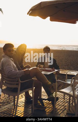 Eine Gruppe von Freunden genießt gerne einen wunderschönen Sonnenuntergang in einem gemütlichen Strandcafé Stockfoto