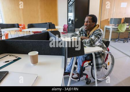 Mann im Rollstuhl, der im Büro sitzt Stockfoto