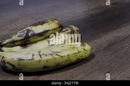 Bild von drei Bananen in einer braunen Schale auf hölzernem Hintergrund. Stockfoto