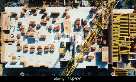 Luftaufnahme der Baustelle mit Kran und Baumaterialien. Eine Luftaufnahme einer Baustelle mit Stapeln von Baumaterialien und einem Stockfoto
