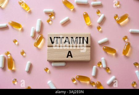 Vitamin-A-Symbol. Konzeptwort Vitamin A auf Holzblöcken. Schöner rosafarbener Hintergrund mit Pillen. Medizin und Vitamin-A-Konzept. Kopierbereich Stockfoto