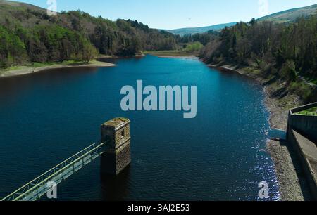 Aus der Vogelperspektive auf einen tiefblauen Stausee umgeben von dichtem Wald. Ein steinerner Turm mit einem Fußweg erstreckt sich in ruhiges Wasser. Stockfoto