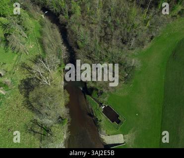 Eine Luftaufnahme von oben zeigt den Fluss, der durch eine lebhafte grüne Landschaft mit Bäumen am Ufer verläuft. In der Nähe des Flusses ist eine kleine Struktur zu sehen Stockfoto