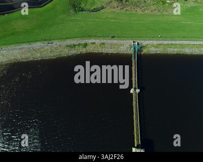 Minimalistischer Blick von oben auf einen langen Pier, der sich in einen dunklen See erstreckt Stockfoto