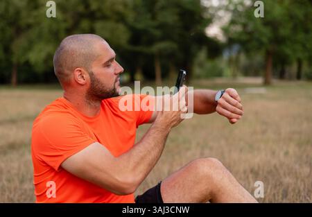 Sportlicher Mann, der die Ergebnisse des Laufens an einer Smart Watch und einem Smartphone überprüft. Stockfoto