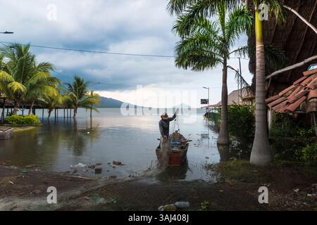 Fischer arrangieren seine Fischernetze an der überfluteten Küste von Puerto Momotombo. Momotombito Island im Hintergrund und wolkenbedeckter Vulkan Momotombo links Stockfoto