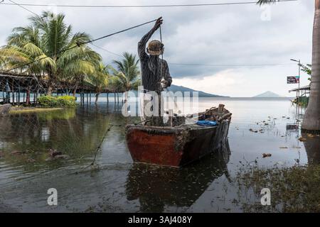 Fischer arrangieren seine Fischernetze an der überfluteten Küste von Puerto Momotombo. Momotombito Island im Hintergrund und wolkenbedeckter Vulkan Momotombo links Stockfoto