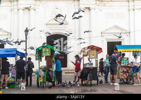Straßenverkäufer, fliegende Tauben und Menschen vor der Kathedrale von Leon. Leon, Nicaragua. Stockfoto